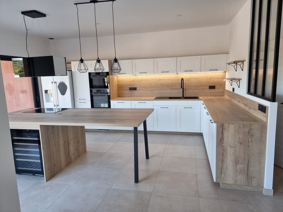 Cuisine moderne blanche et bois avec îlot central, cave à vin et luminaires noirs suspendus.
