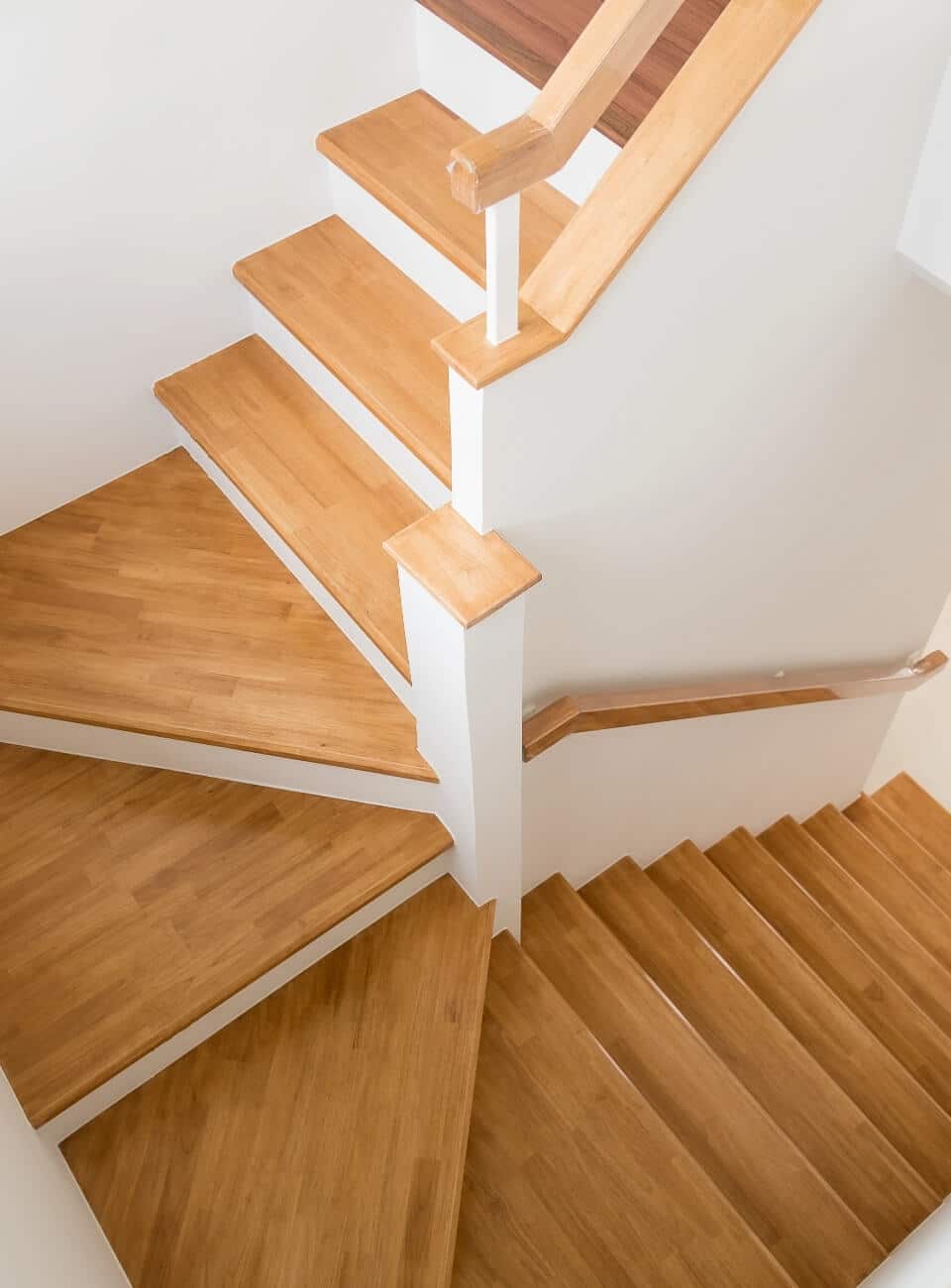 Escalier tournant en bois clair moderne avec contremarches blanches et rampe élégante vue de haut.